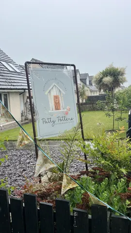 A sign for a gardening business is hanging on a metal pole.