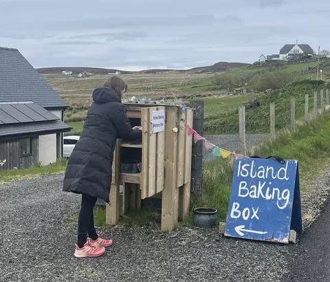 A woman is standing in front of a wooden box with a sign that says "Island Baking Box."