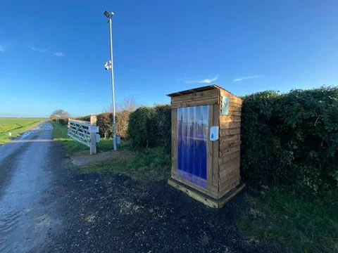 A wooden outhouse is located on the side of a road.