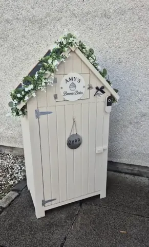 A white wooden shed with a sign that says "Amy's Barn".