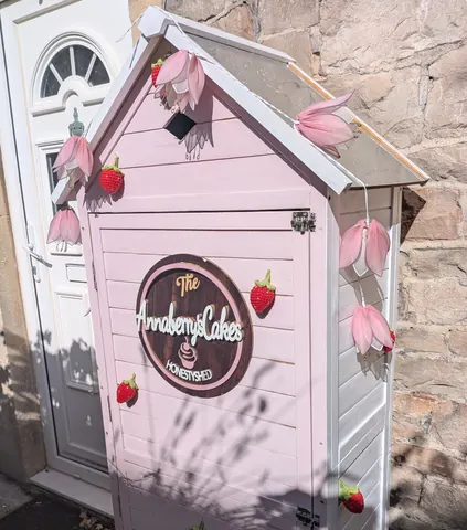 A small pink shed with a sign that says "The Amberly Lakes".