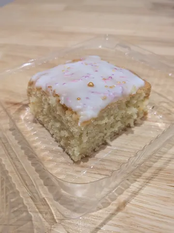 A piece of cake with white frosting and pink sprinkles.