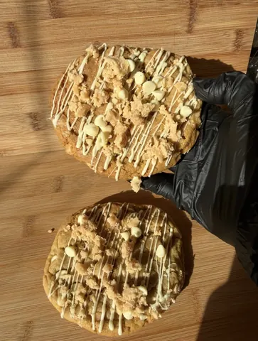 A person is holding a cookie with white icing and chocolate chips.