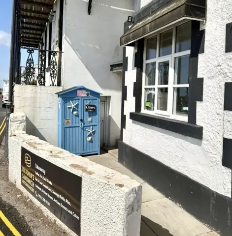 A blue shed is located in front of a white building.