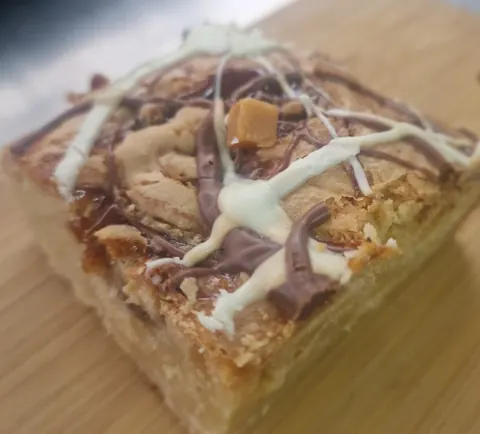 A piece of cake with white icing and chocolate drizzle on a wooden table.