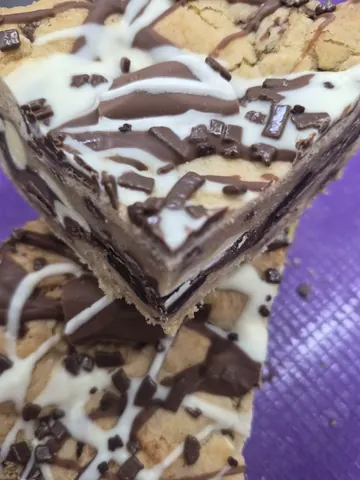 A piece of chocolate and white cake with chocolate drizzled on top.