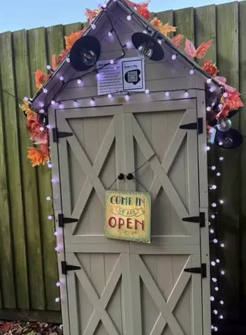A small shed with a sign that says "come in" and lights around it.