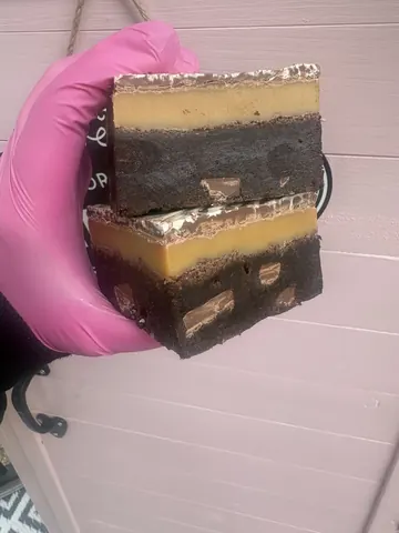 A pink glove holding a square of chocolate cake.