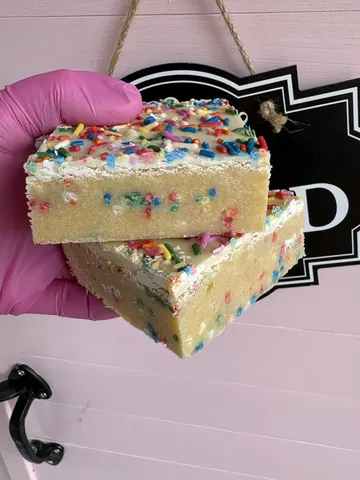 A hand holding a piece of cake with sprinkles.