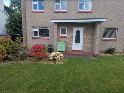 A house with a green door and a red bush in front of it.