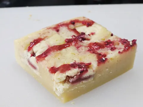 A square of cake with red jelly on top.