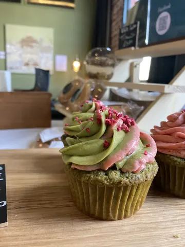 A cupcake with green frosting and pink sprinkles.