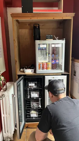 A man is looking at a refrigerator with a lot of drinks in it.