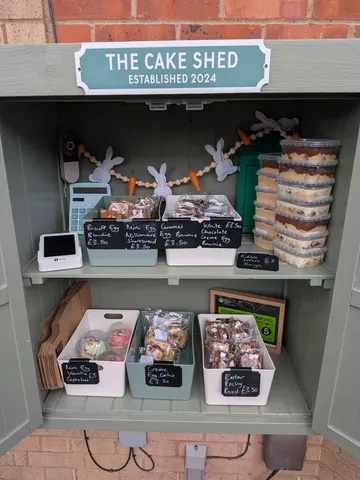 A small green building with a sign that says "The Cake Shed" on it.