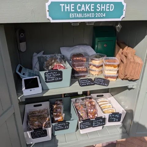 A small wooden shack with a sign that says "The Cake Shed" on it.