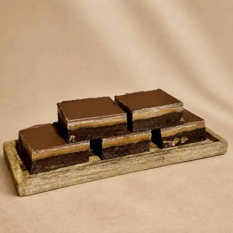A wooden tray with a square of chocolate cake on it.