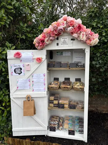 A white wooden structure with a pink flower display and a shelf full of pastries.
