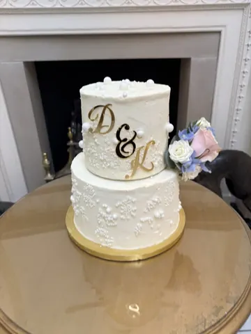 A white cake with gold trim and a pink flower on top.