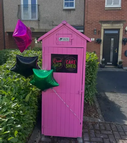 A pink shed with balloons hanging from it.