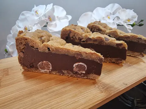 A piece of chocolate cake with chocolate chips on a wooden table.
