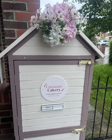 A small white building with a pink door and a sign that says Cussons Cake Cakery.