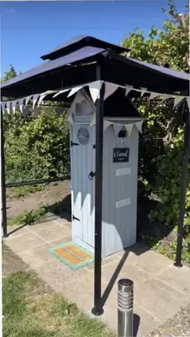 A small white building with a black roof and a sign on the door.