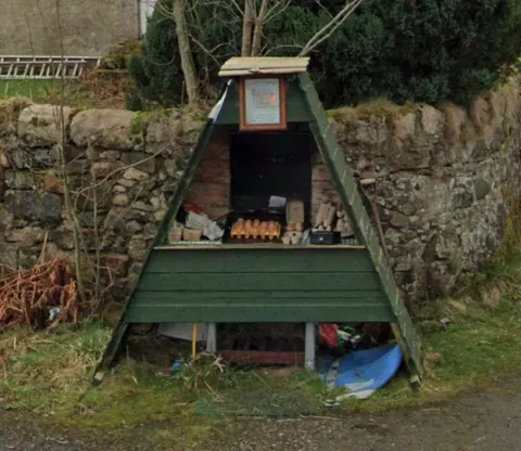 A small green building with a roof and a sign on it.