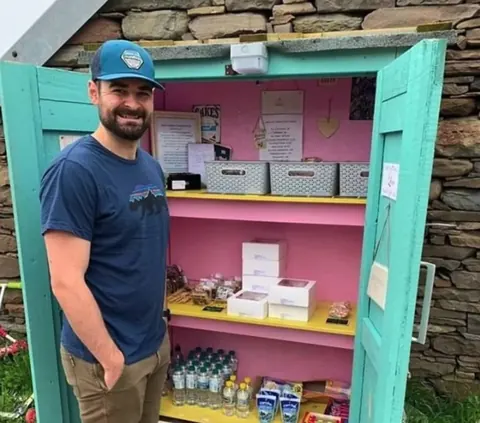 A man is standing in front of a pink and blue door.