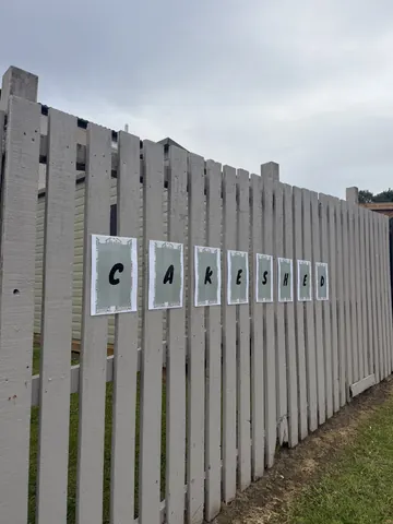 A white fence with a sign that says "Cakes" on it.