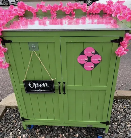 A green cabinet with a pink flower decoration on the top.
