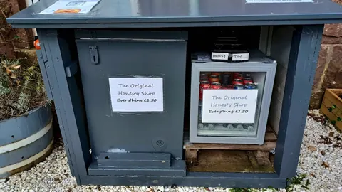 A small refrigerator with a sign on the door that says "The Original Honesty Shop".