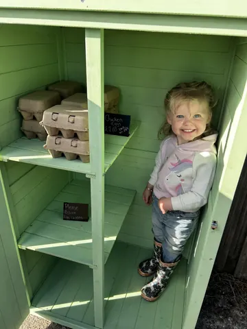 A little girl is standing inside a green cabinet.