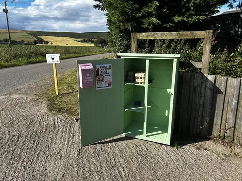 A small green shed with a pink sign on the side of a road.
