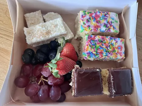 A box of food with a strawberry, grapes, and cake.