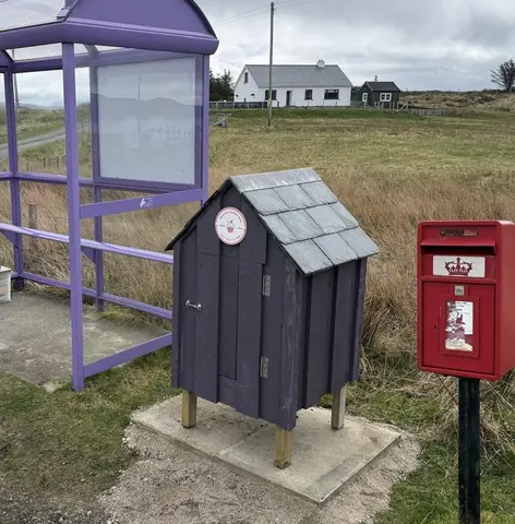 A purple and white bus stop with a clock on the side.