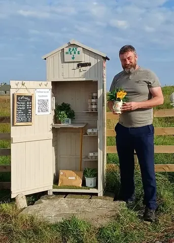 A man is standing next to a small white shed.