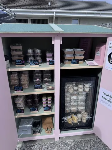 A pink food stand with a refrigerator and a sign.