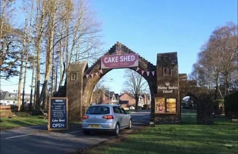 A car is parked in front of a sign that says "Cake Shed."