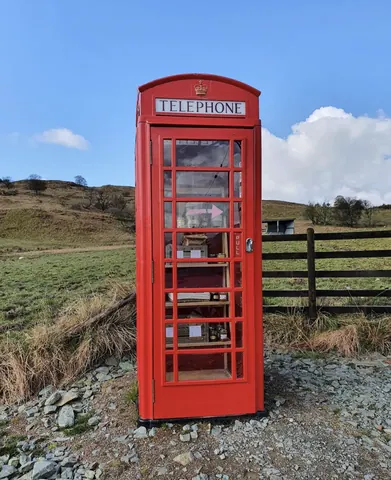 A red telephone booth is sitting in a field.