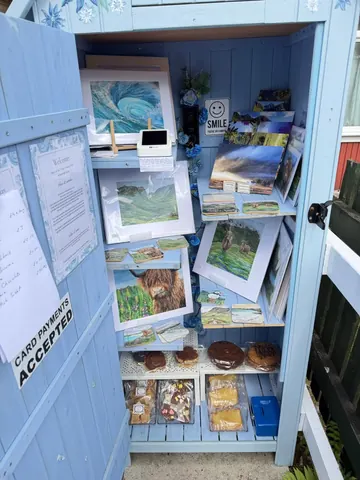 A blue shed with a sign that says "card accepted" and a shelf with pictures and food items.