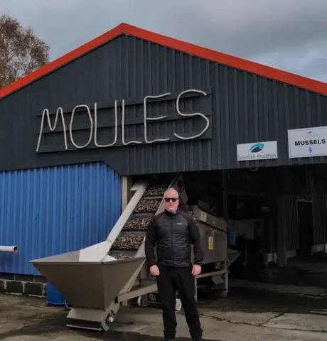 A man standing in front of a building with the word Moulis on it.