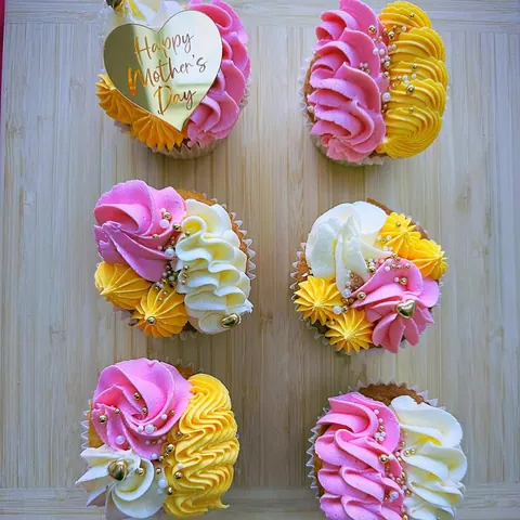 A table with a gold heart and six cupcakes with pink and yellow frosting.