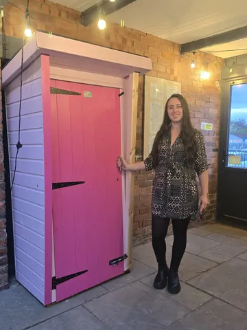 A woman is standing in front of a pink door.