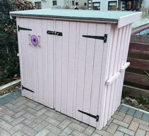 A pink shed with a purple flower on it.