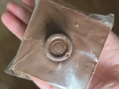 A hand holding a piece of chocolate with a hole in it.