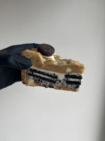 A person is holding a piece of cake with a cookie on top.