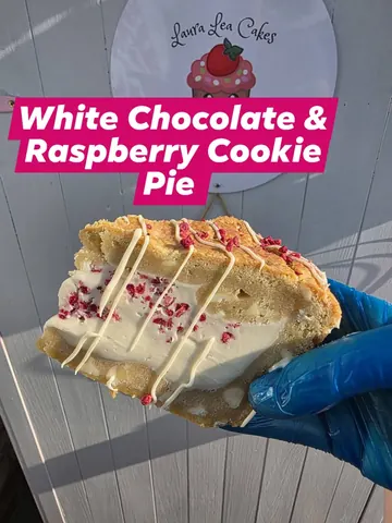 A person is holding a piece of cake with white chocolate and raspberry topping.