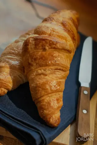 A knife is on a table next to a croissant.
