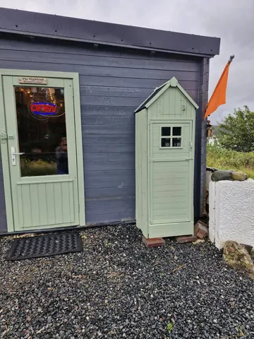 A small green shed is sitting next to a blue door.
