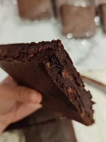 A person is holding a piece of chocolate cake.